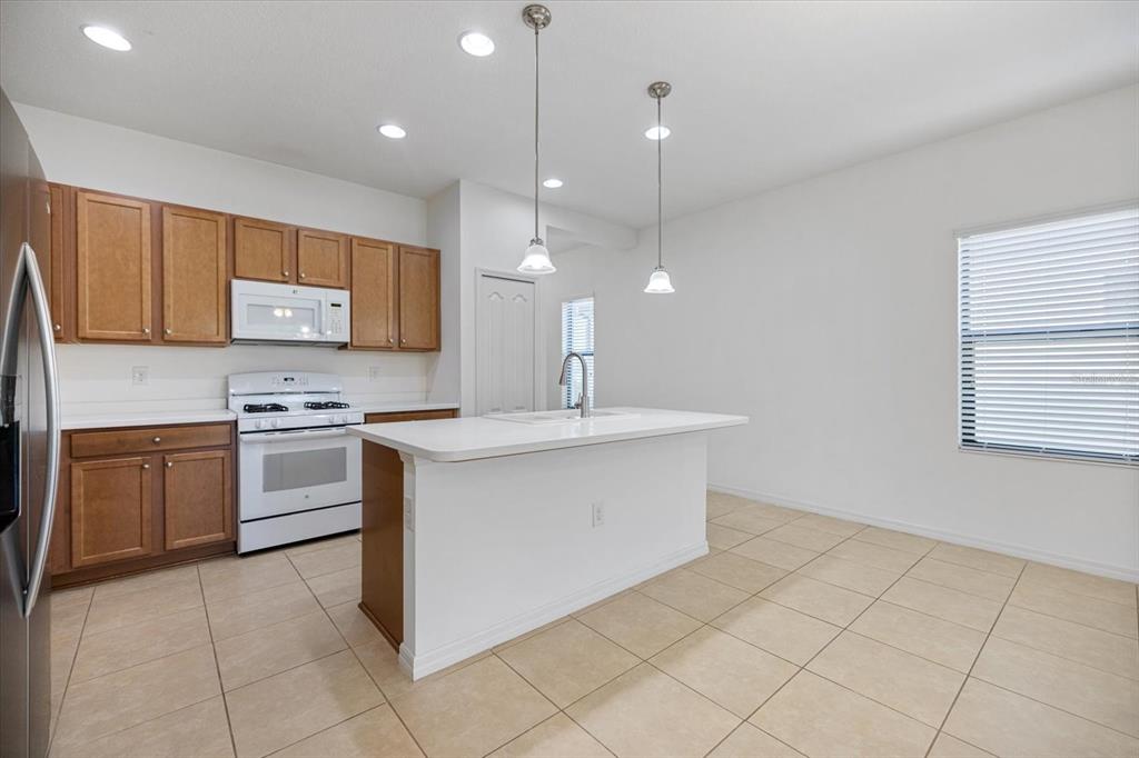 A kitchen features wood cabinets, white appliances, a central island, and light-colored tile flooring — 229 LIVORNO WAY, NOKOMIS, FL