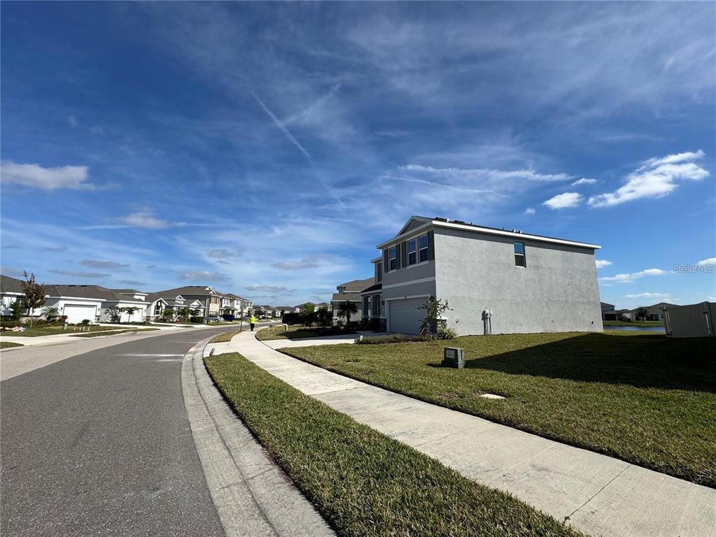 A two-story suburban house with a gray stucco exterior stands beside a paved street — 17710 CANTARINA COVE, BRADENTON, FL