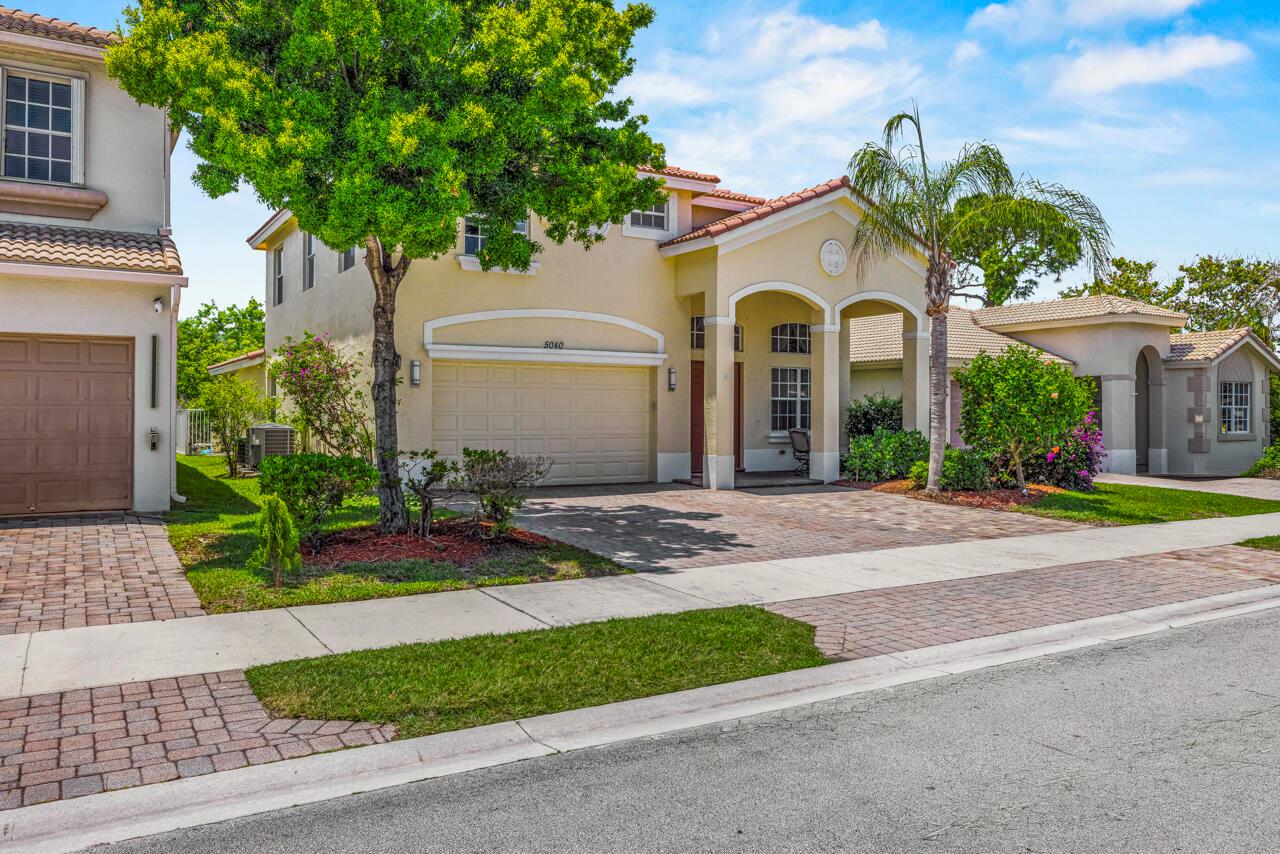 A two-story suburban house with a beige stucco exterior, a two-car garage, and a palm tree — 5040 SE Graham Drive, Stuart FL 34997, STUART, FL