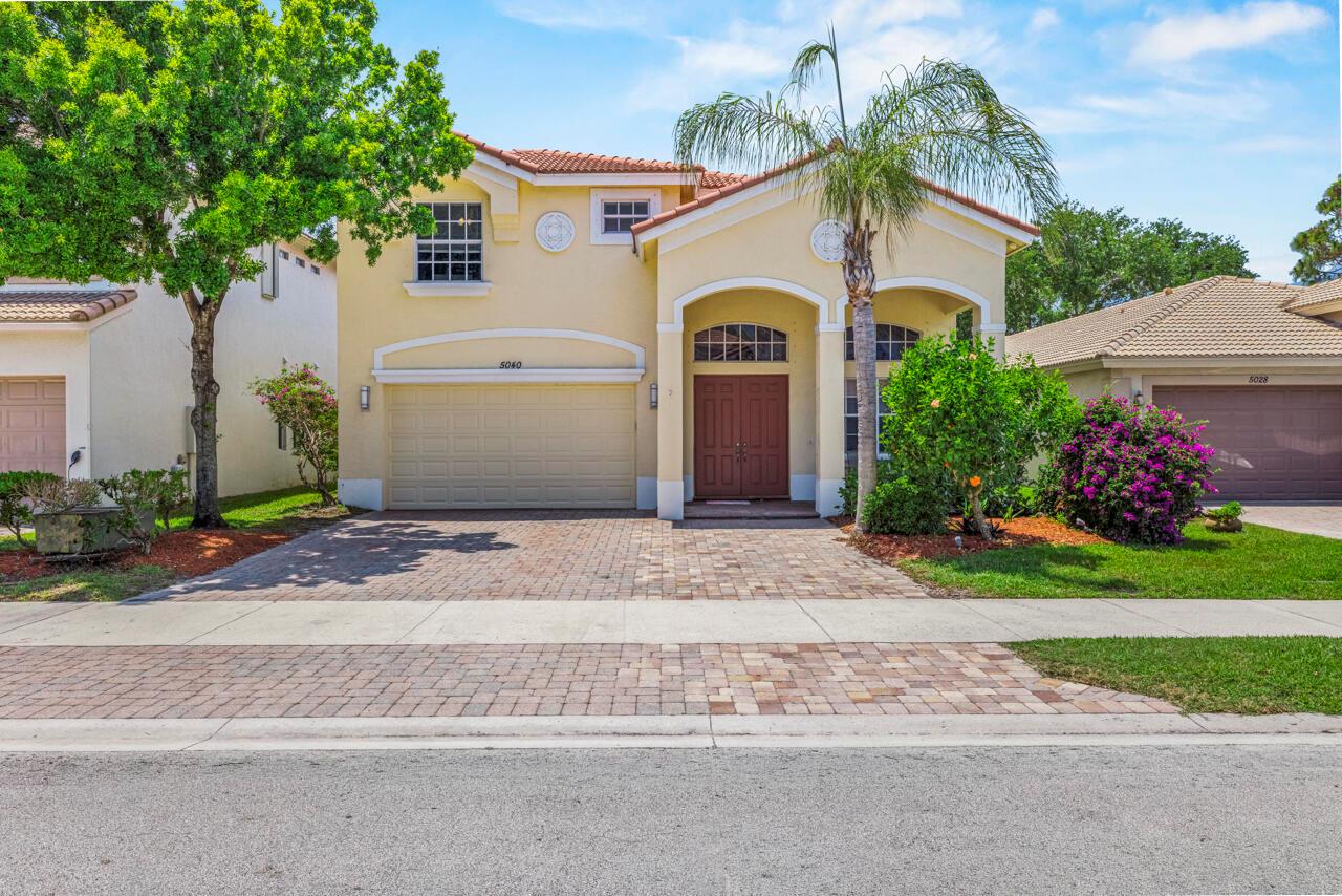 A two-story yellow stucco house with a paved driveway, arched entryway, and a palm tree — 5040 SE Graham Drive, Stuart FL 34997, STUART, FL