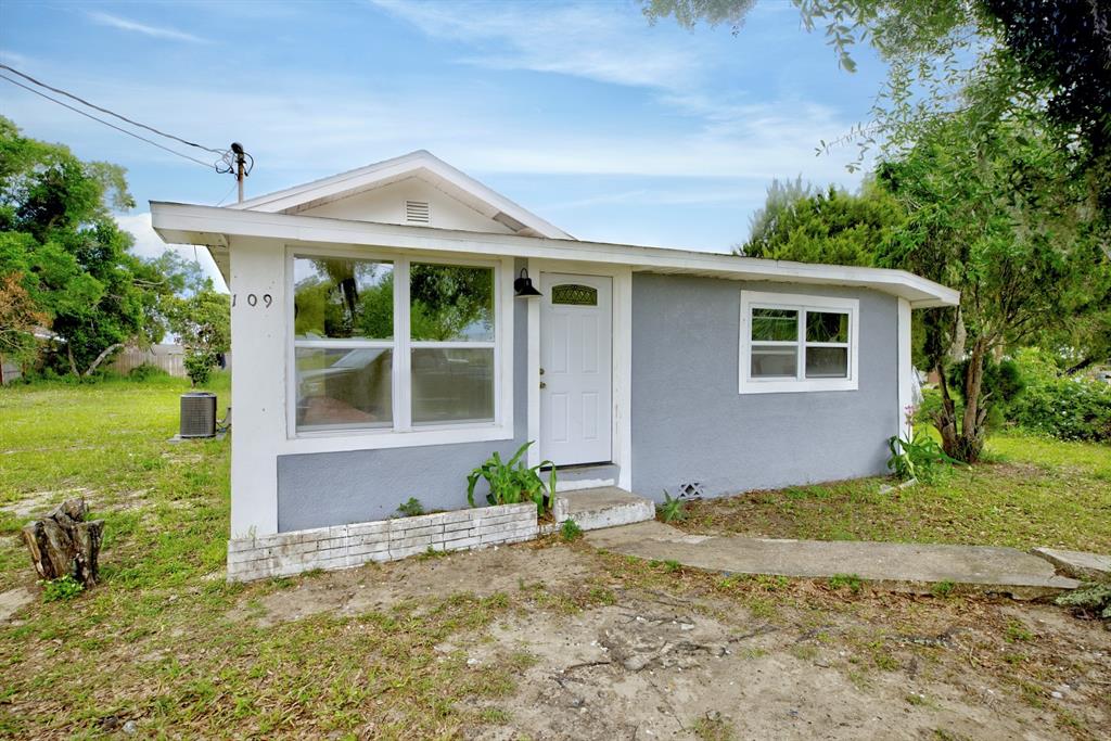 A small, gray, single-story house with a white door and a large front window — 109 S ANOKA AVENUE, AVON PARK, FL