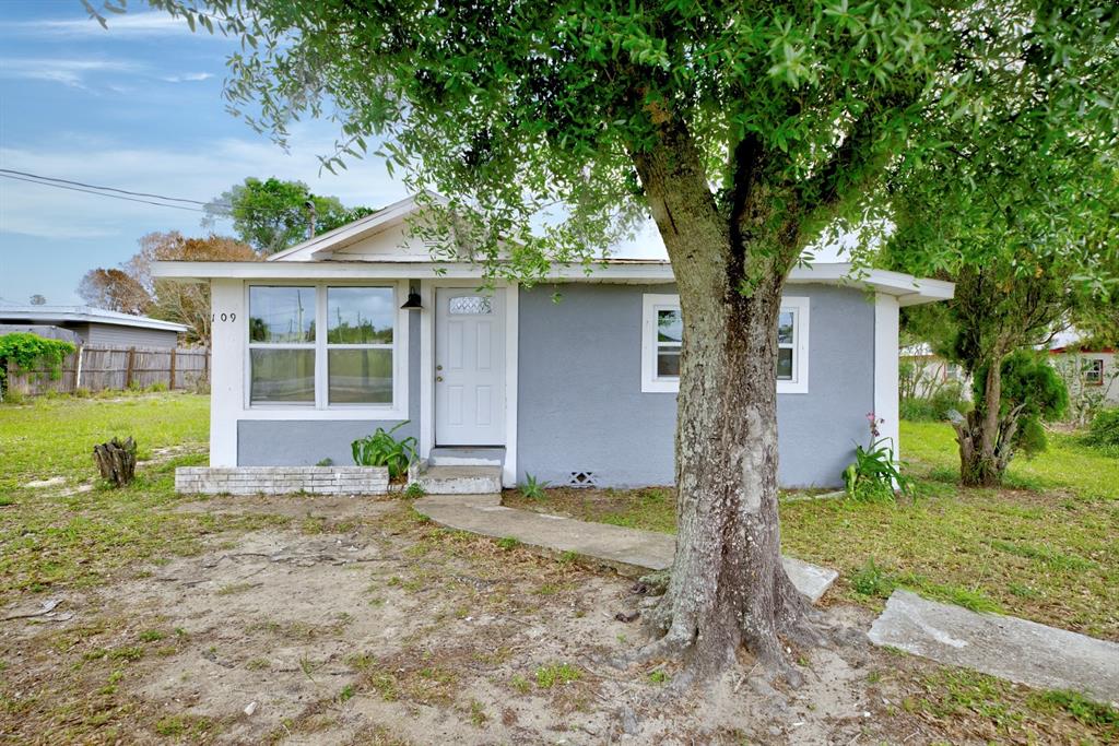 A small, gray, single-story house with a white front door and a large tree — 109 S ANOKA AVENUE, AVON PARK, FL