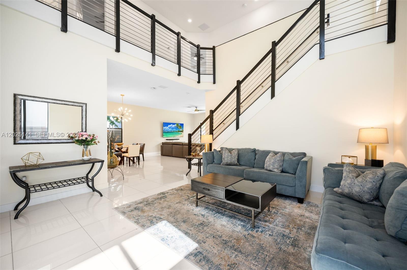 A high-ceilinged living room features a staircase with a metal railing and tile flooring — 8763 NW 157th Ter, Miami Lakes FL 33018, MIAMI LAKES, FL