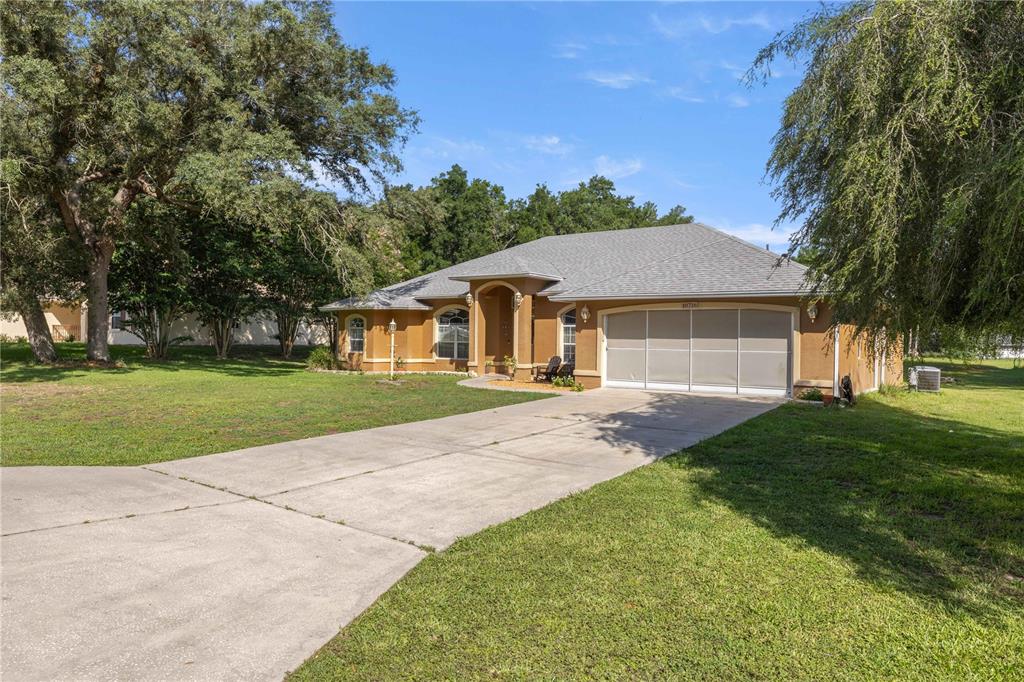 A single-story tan stucco house with a gray shingled roof and a concrete driveway — 10716 SW 53RD CIRCLE, OCALA, FL