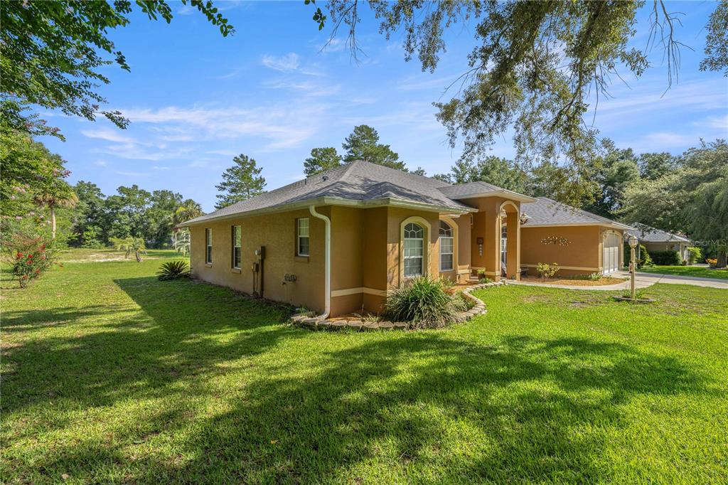 A side view of a tan stucco house with a hip roof and green lawn — 10716 SW 53RD CIRCLE, OCALA, FL
