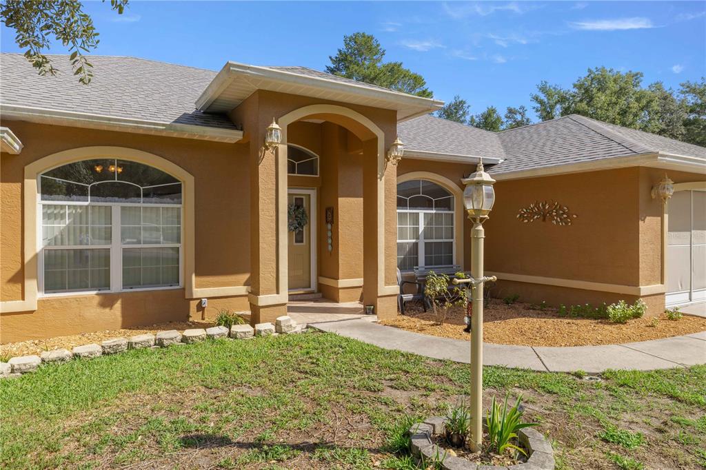 A tan stucco house with a covered entryway, arched windows, and a front yard lamp — 10716 SW 53RD CIRCLE, OCALA, FL