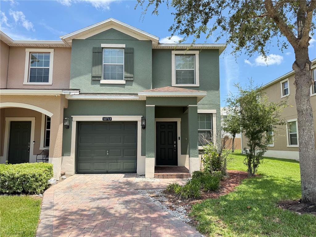 A two-story townhouse with a green stucco exterior, a single-car garage, and a paved driveway — 10713 SAVANNAH LANDING CIRCLE, ORLANDO, FL