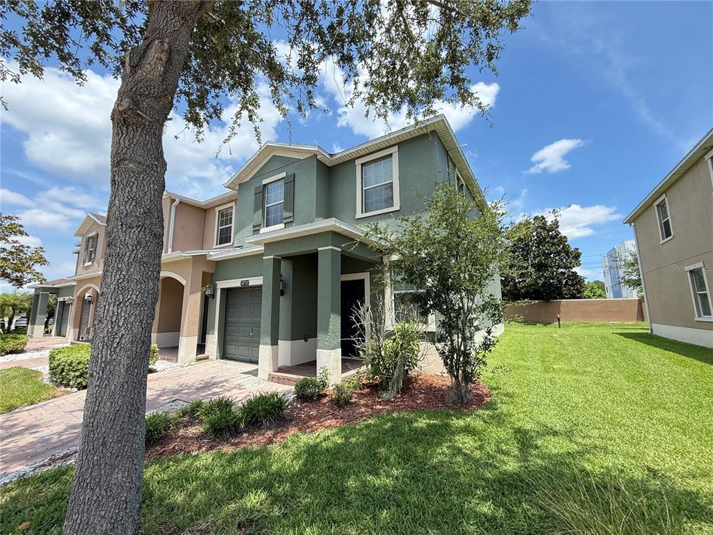 A two-story green townhouse with a brick driveway and a side yard — 10713 SAVANNAH LANDING CIRCLE, ORLANDO, FL