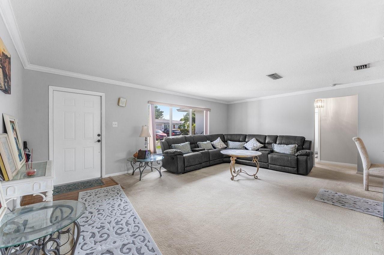 A living room features a large gray sectional sofa, beige carpeting, and a white door — 745 NW 72nd Terrace, Margate FL 33063, MARGATE, FL
