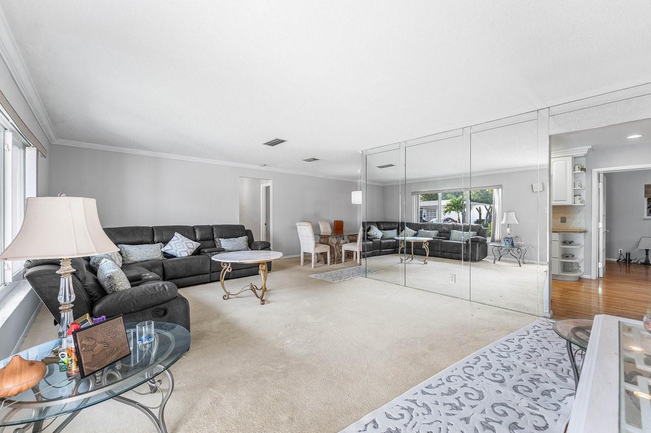A living room with beige carpeting, a dark leather sofa, and a large mirrored wall — 745 NW 72nd Terrace, Margate FL 33063, MARGATE, FL