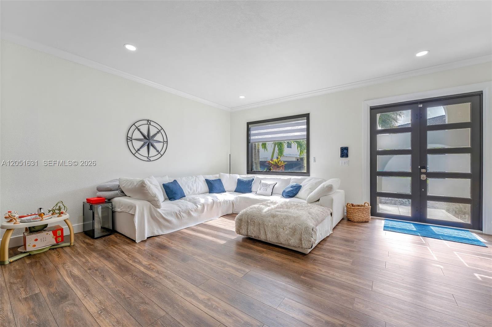 A living room features a white sectional sofa, wood-look flooring, and a dark-framed glass door — 27260 SW 136th Path, Homestead FL 33032, HOMESTEAD, FL