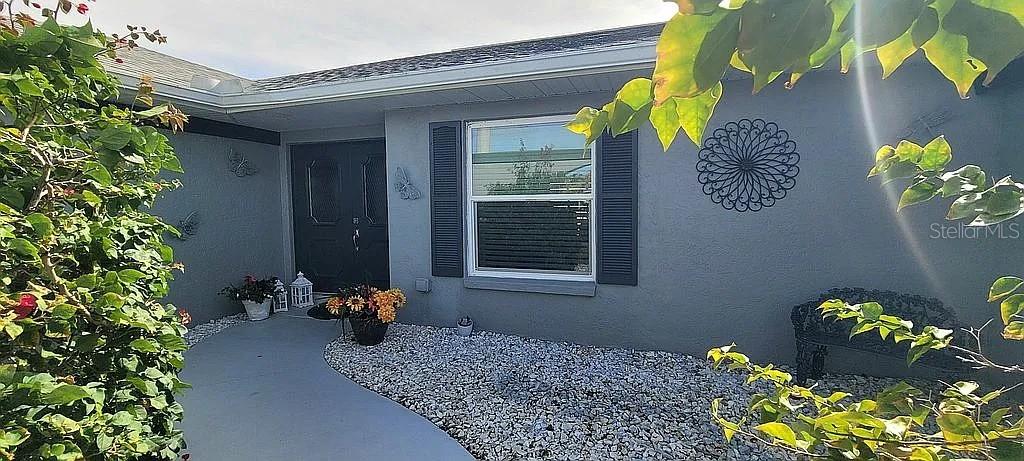 A gray house exterior features a front door, a window with shutters, and gravel landscaping — 1840 FLAMETREE LANE, VENICE, FL