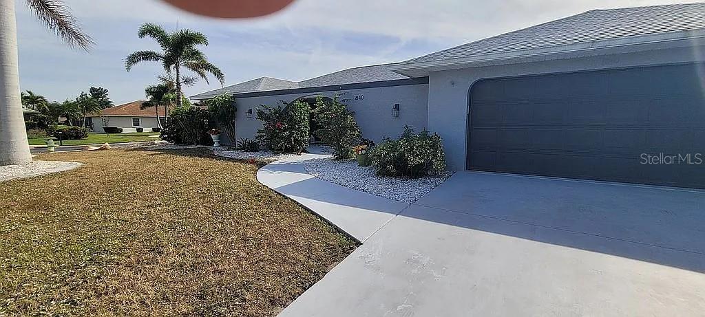 A light gray house features a large garage, a curved walkway, and landscaped front bushes — 1840 FLAMETREE LANE, VENICE, FL