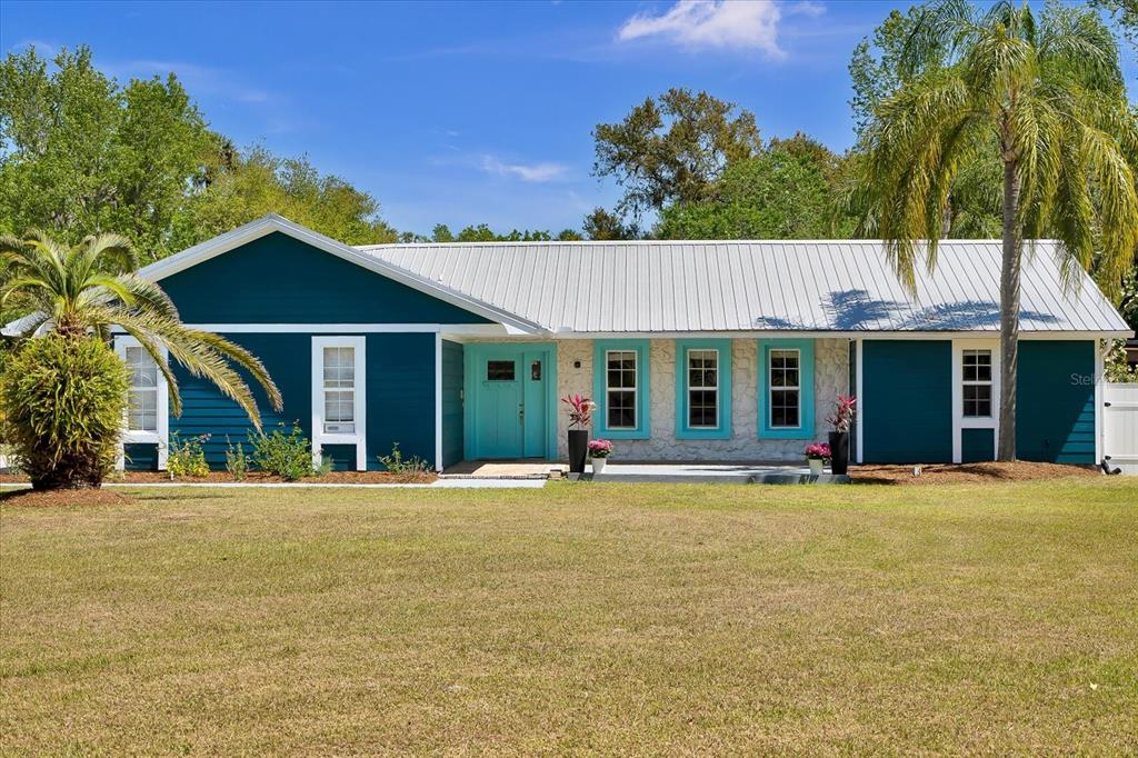 A single-story house with teal siding, a metal roof, and a stone facade exterior — 245 COUNTRY CIRCLE DRIVE E, PORT ORANGE, FL