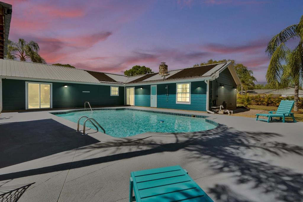 A teal house with a metal roof overlooks a backyard swimming pool and patio area — 245 COUNTRY CIRCLE DRIVE E, PORT ORANGE, FL