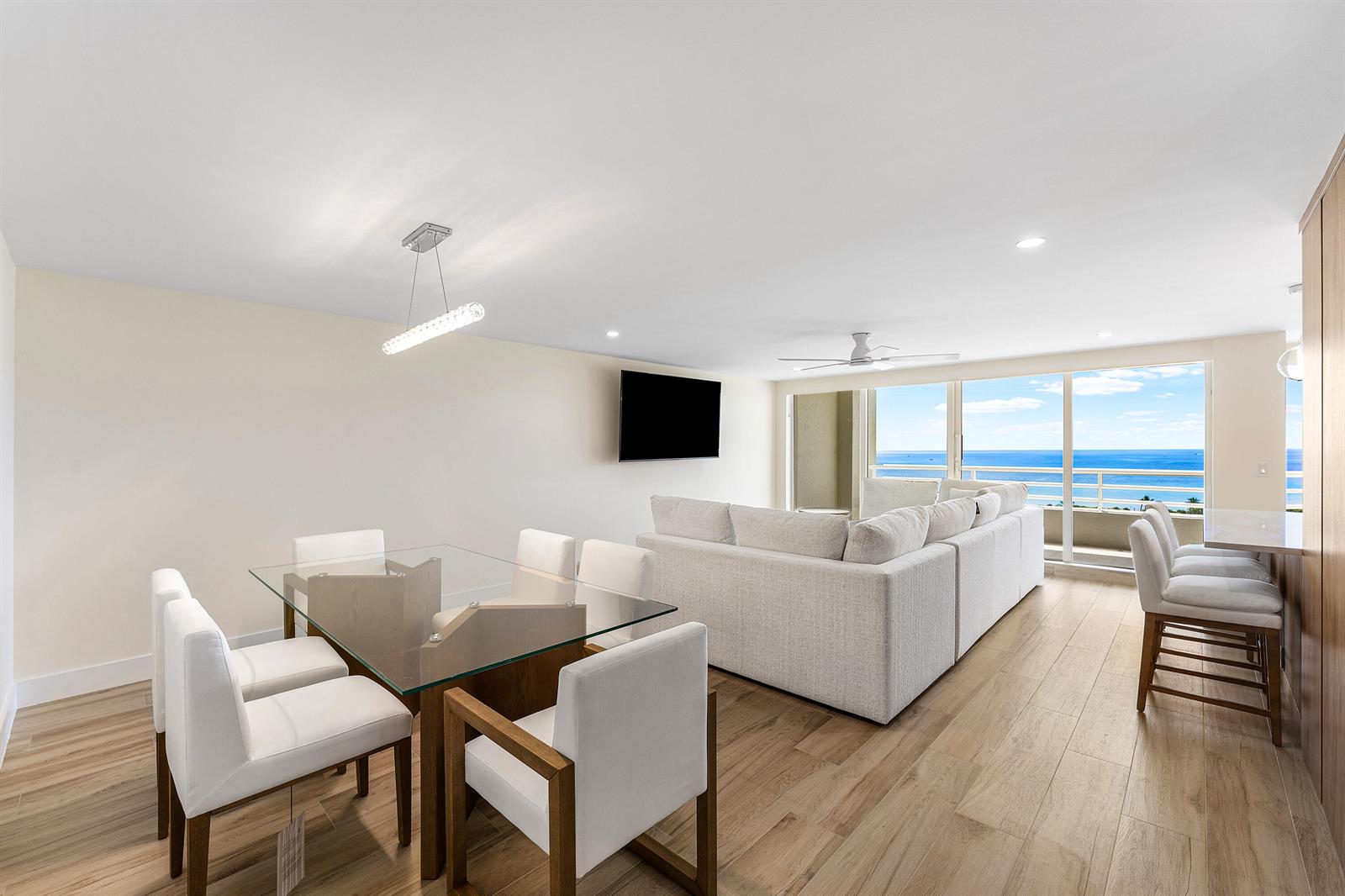 A bright, open-concept living and dining area features light wood floors, white furniture, and ocean views — 4201 Ocean Boulevard # 1407, Boca Raton FL 33431, BOCA RATON, FL