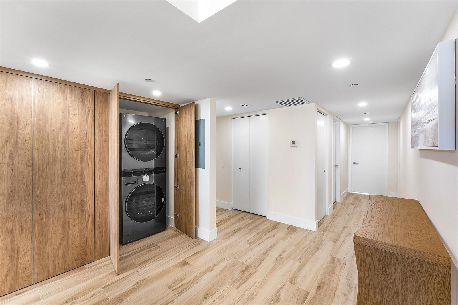 A hallway features wood-look tile flooring, a stacked laundry unit in a closet, and white doors — 4201 Ocean Boulevard # 1407, Boca Raton FL 33431, BOCA RATON, FL