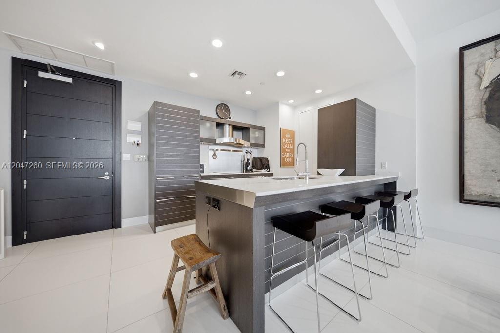 A modern kitchen features dark wood cabinetry, a white stone island, and four bar stools — 200 Biscayne Boulevard Way # 5110, Miami FL 33131, MIAMI, FL