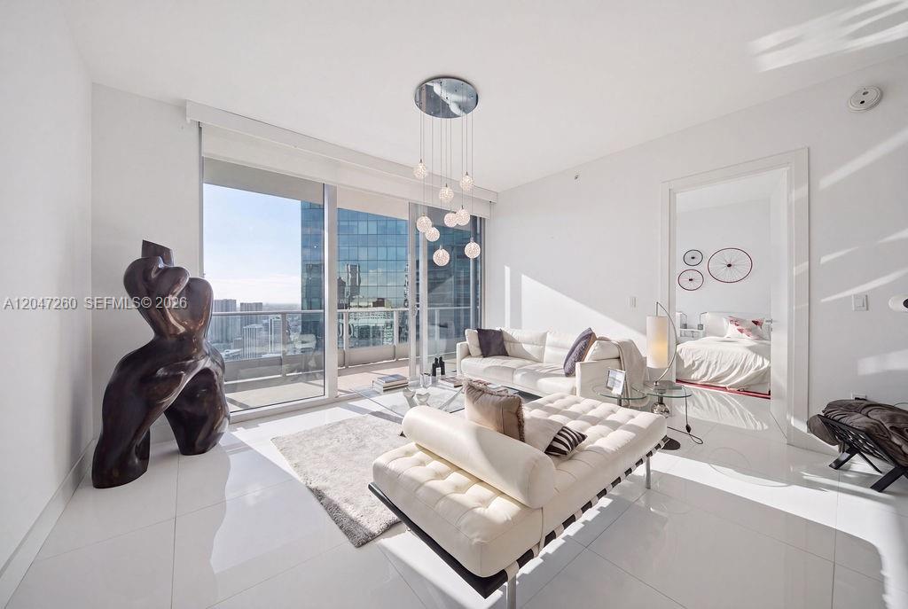 A bright living room features white tile floors, a modern chandelier, and floor-to-ceiling windows — 200 Biscayne Boulevard Way # 5110, Miami FL 33131, MIAMI, FL