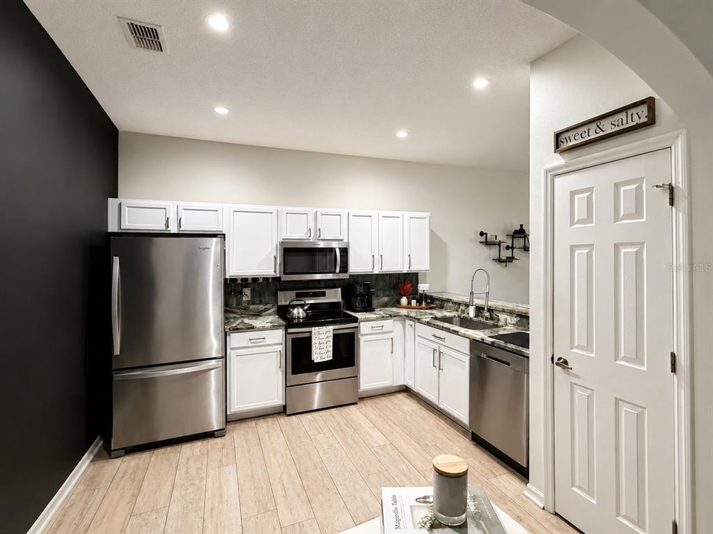 A kitchen features white cabinets, stainless steel appliances, a black accent wall, and wood-look flooring — 2029 SHULLER WAY, CASSELBERRY, FL