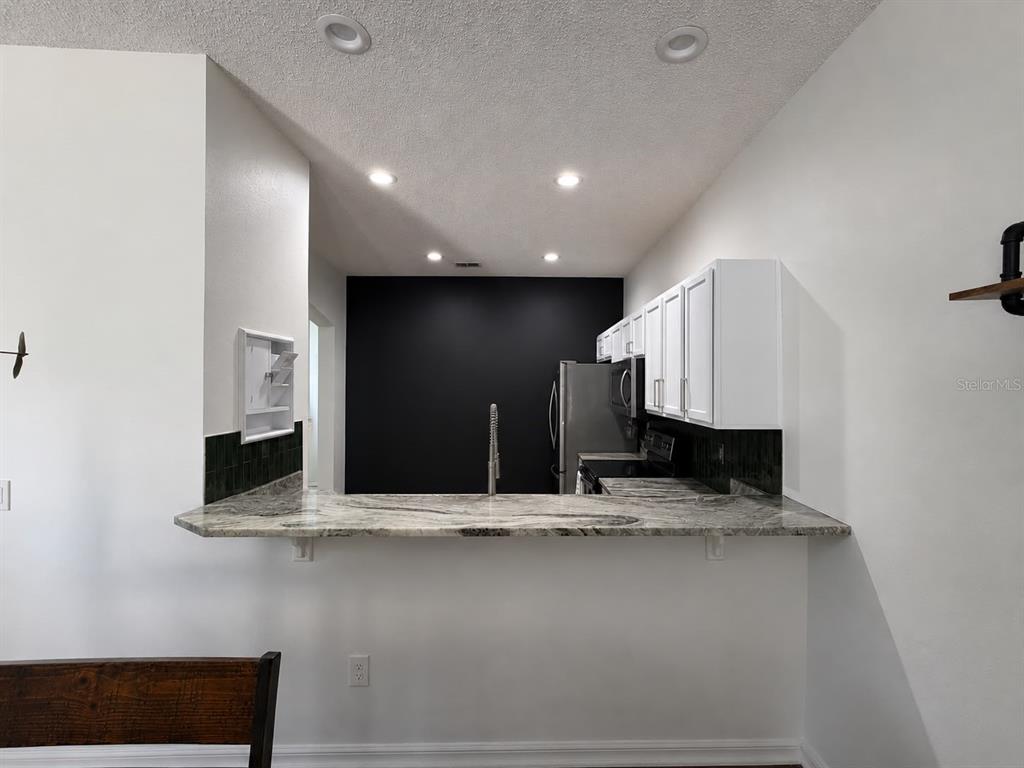 A kitchen features white cabinets, a marble-patterned breakfast bar, and a black accent wall — 2029 SHULLER WAY, CASSELBERRY, FL