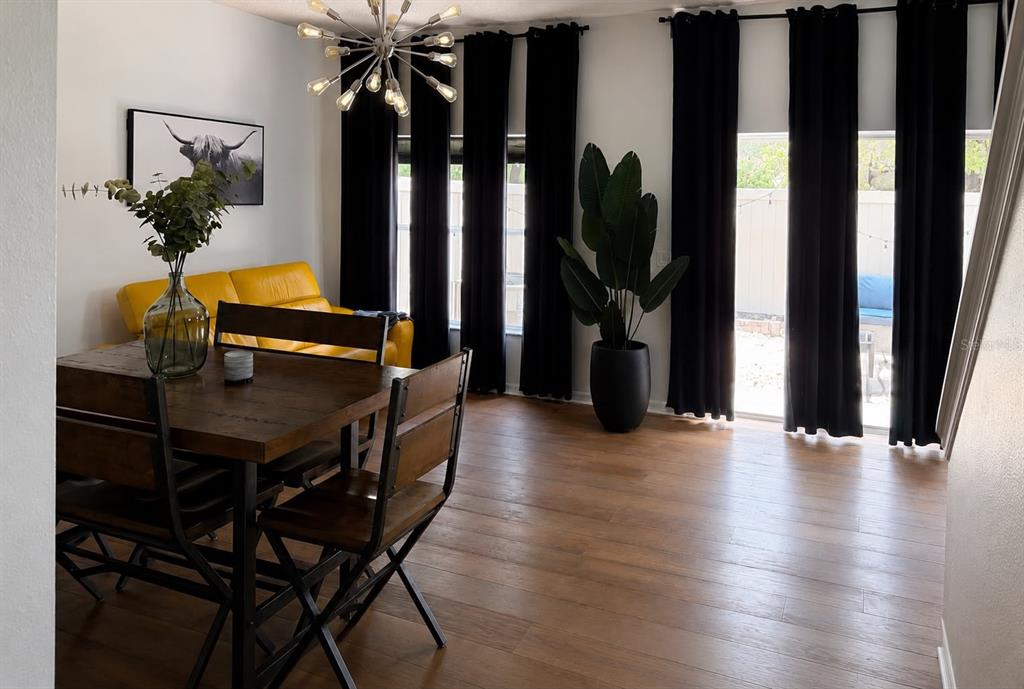 A dining area with a wooden table, yellow sofa, and black curtains on large windows — 2029 SHULLER WAY, CASSELBERRY, FL