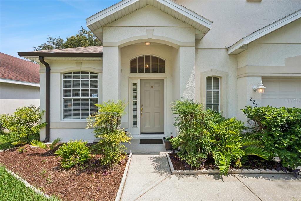The exterior of a house features a beige front door, arched window, and landscaped garden — 223 EASTON CIRCLE, OVIEDO, FL