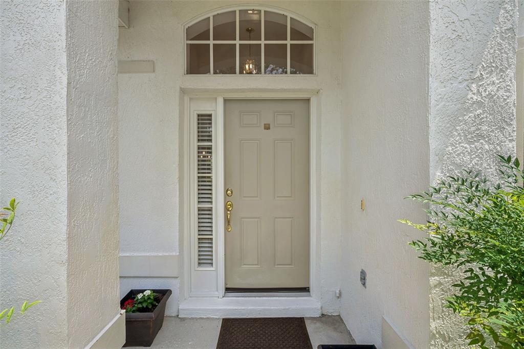 A beige front door with a sidelight and arched transom window sits under a covered entryway — 223 EASTON CIRCLE, OVIEDO, FL
