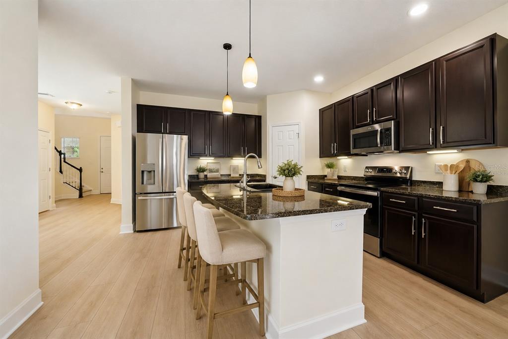 A kitchen features dark wood cabinets, granite countertops, stainless steel appliances, and a breakfast bar — 8418 NANDINA DRIVE, SARASOTA, FL