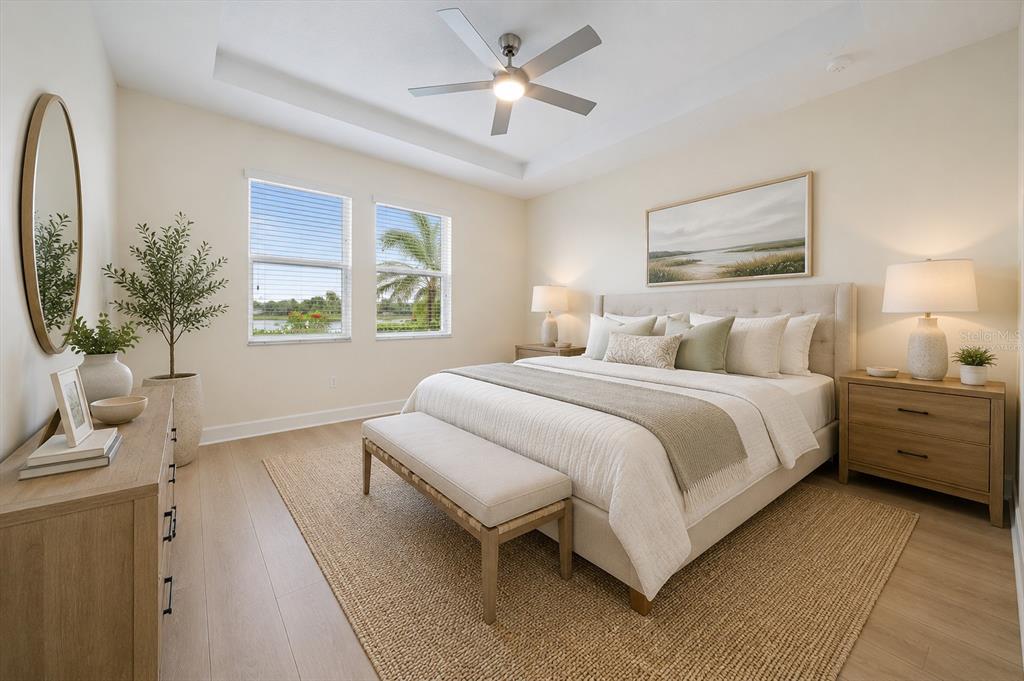 A bright bedroom features a king-sized bed, a ceiling fan, and windows overlooking a lake — 8418 NANDINA DRIVE, SARASOTA, FL