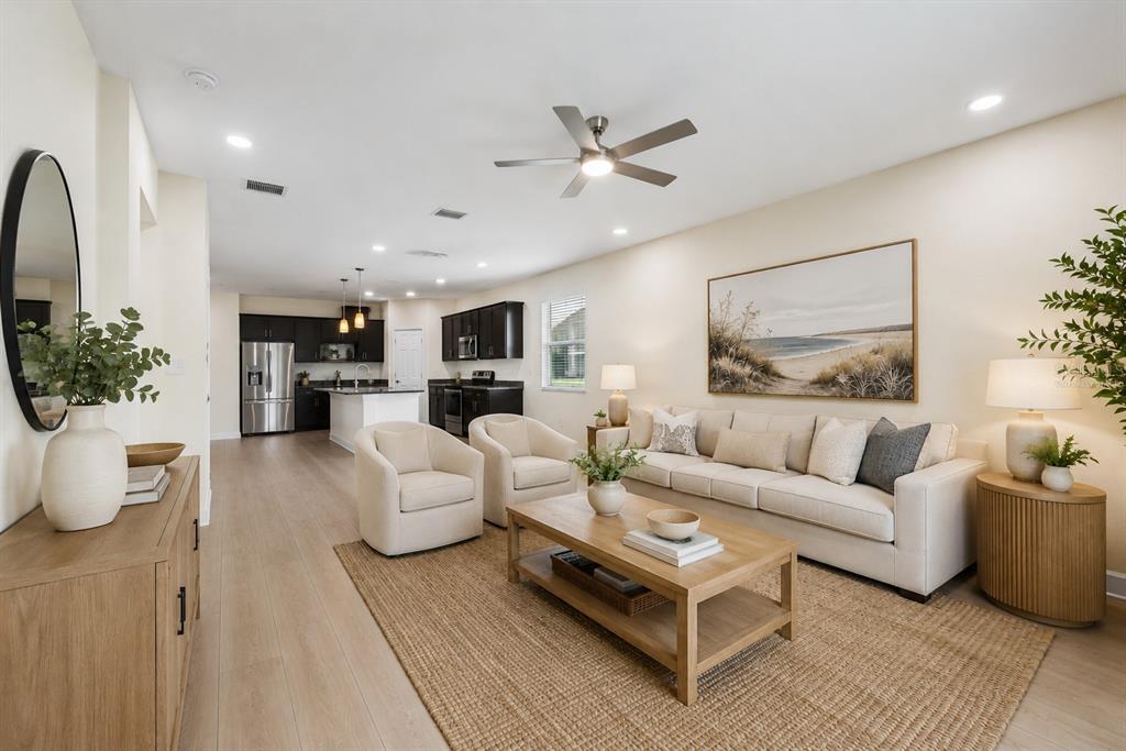 A living room with light wood floors, a beige sofa, two armchairs, and an open kitchen — 8418 NANDINA DRIVE, SARASOTA, FL
