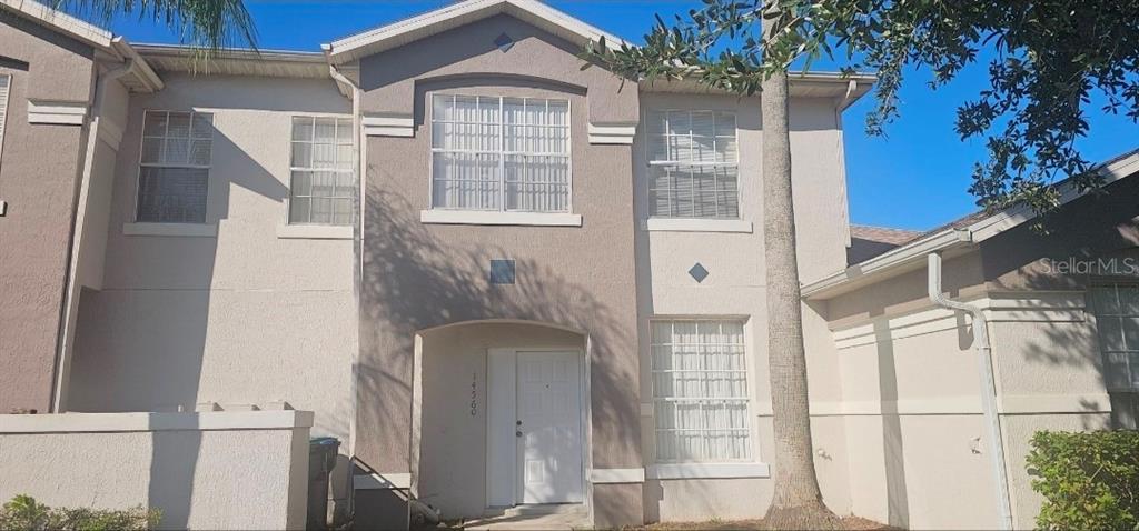 A two-story house exterior features a brown stucco facade, a white front door, and a palm tree — 14560 LAGUNA BEACH CIRCLE, ORLANDO, FL