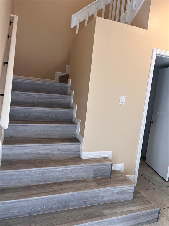 A staircase with wood-look flooring leads upward beside a beige wall and a white door — 14560 LAGUNA BEACH CIRCLE, ORLANDO, FL