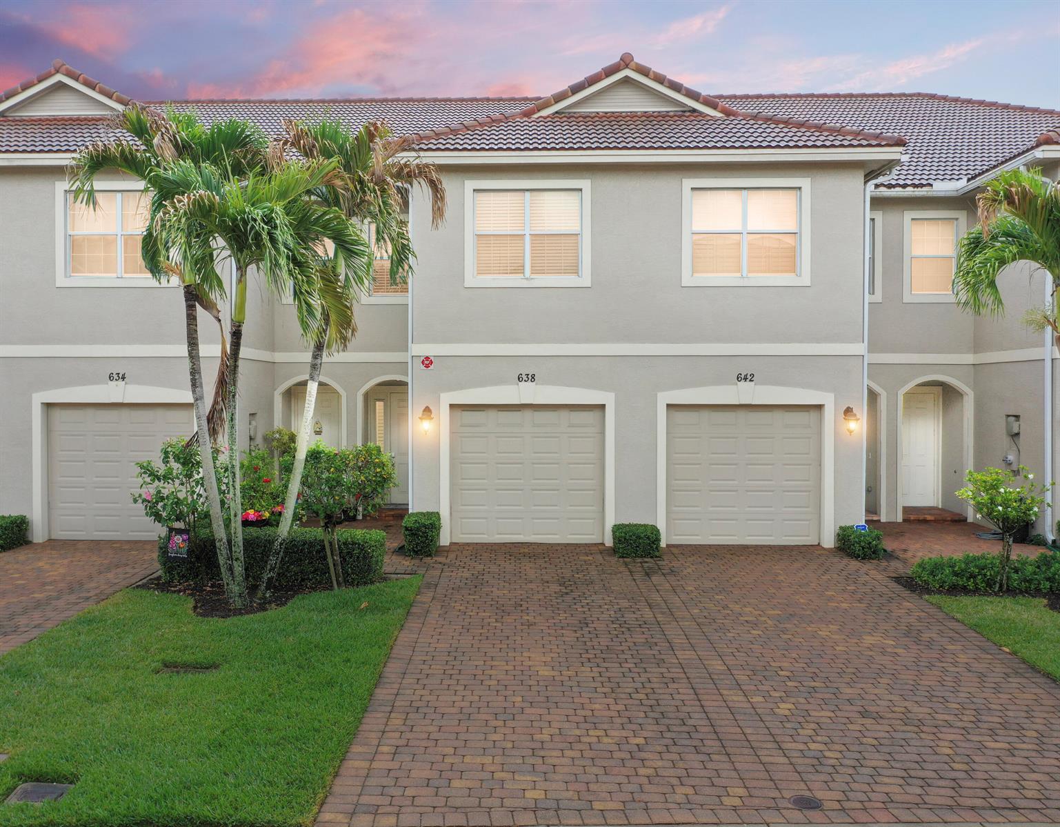 A row of three townhouses with beige stucco exteriors, tiled roofs, and paved driveways at dusk — 638 SW Glen Crest Way, Stuart FL 34997, STUART, FL