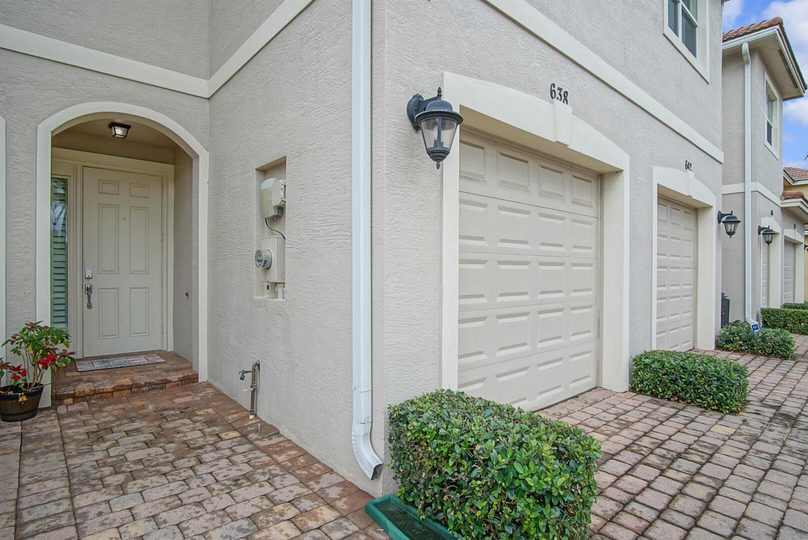 A beige townhouse exterior features a brick paver driveway, a garage, and a front entrance — 638 SW Glen Crest Way, Stuart FL 34997, STUART, FL