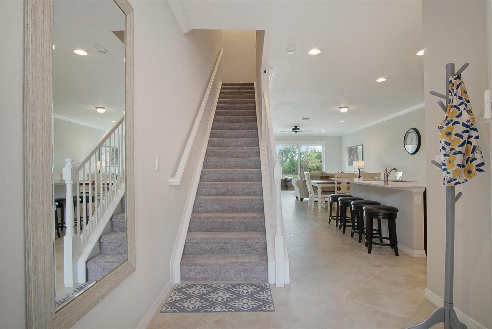 An entryway features a carpeted staircase, a large wall mirror, and a view into the kitchen — 638 SW Glen Crest Way, Stuart FL 34997, STUART, FL