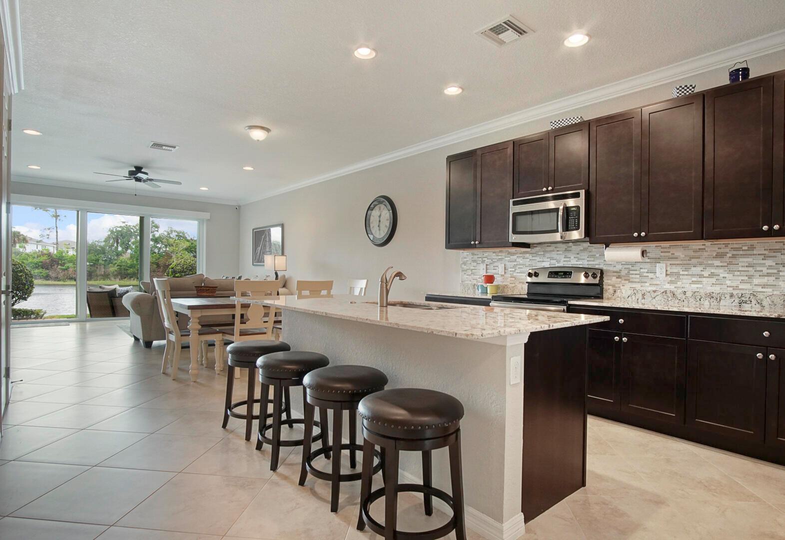 A kitchen with dark wood cabinets and a granite island with bar stools overlooks a dining area — 638 SW Glen Crest Way, Stuart FL 34997, STUART, FL