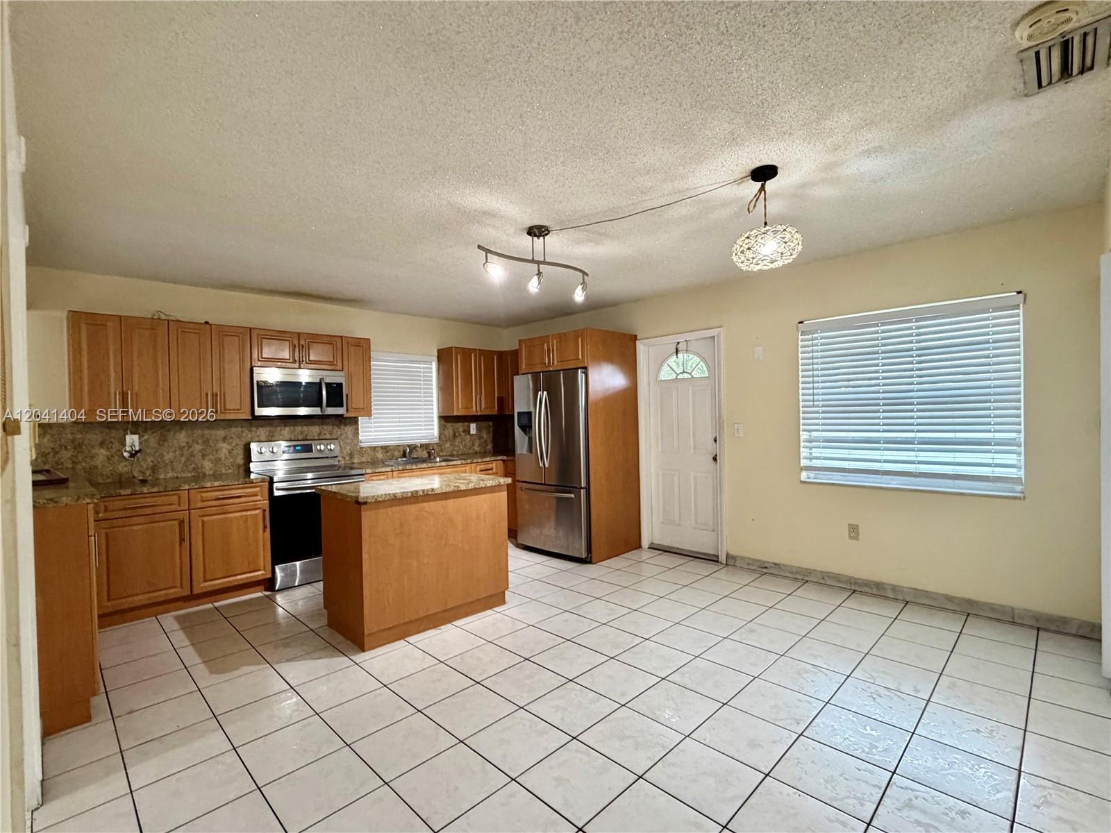 A kitchen features wooden cabinets, stainless steel appliances, a small island, and tiled flooring — 913 NW 22nd Pl # 0, Miami FL 33125, MIAMI, FL