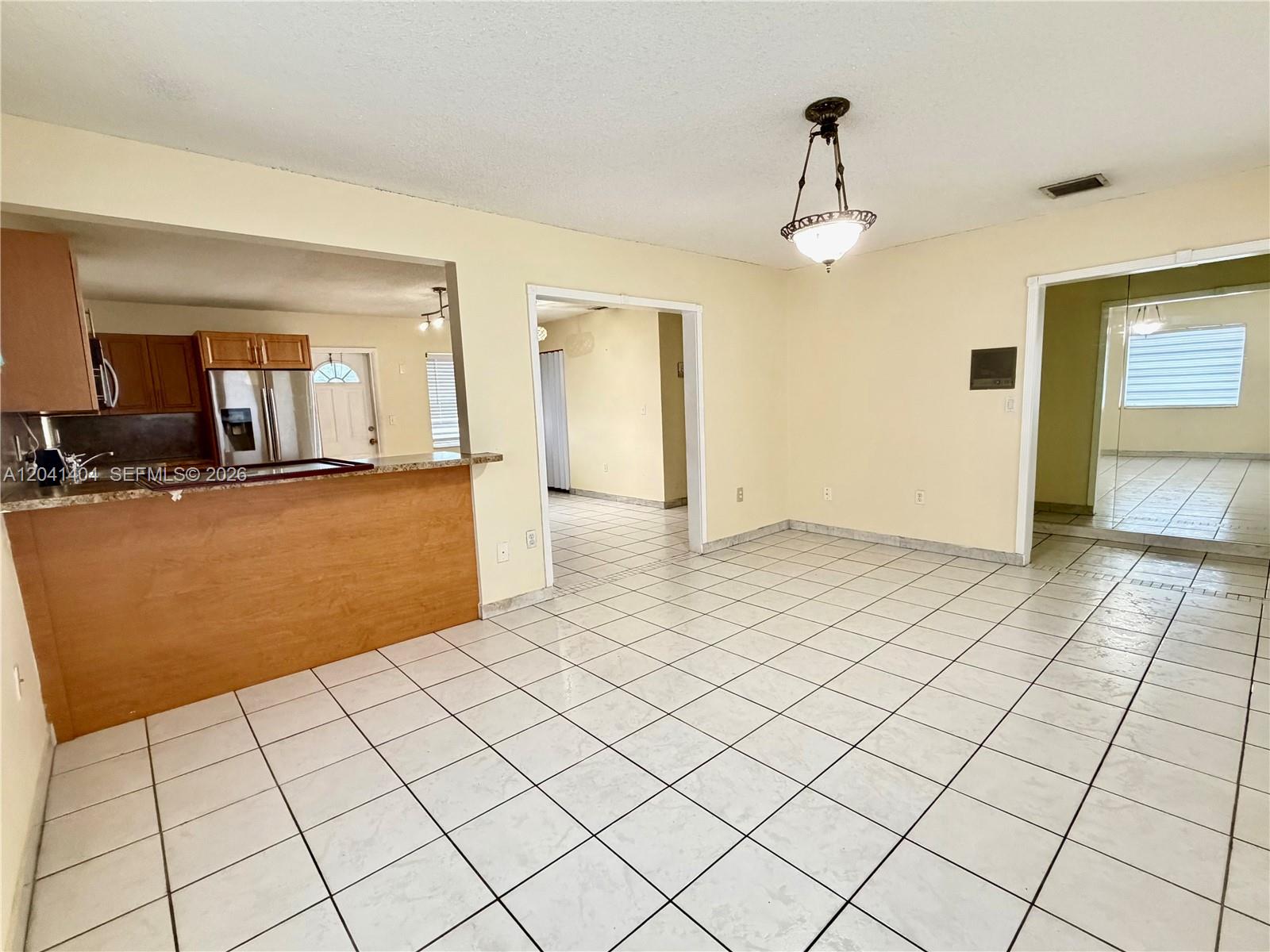 A dining area with white tiled floors features a kitchen pass-through and a hanging light — 913 NW 22nd Pl # 0, Miami FL 33125, MIAMI, FL