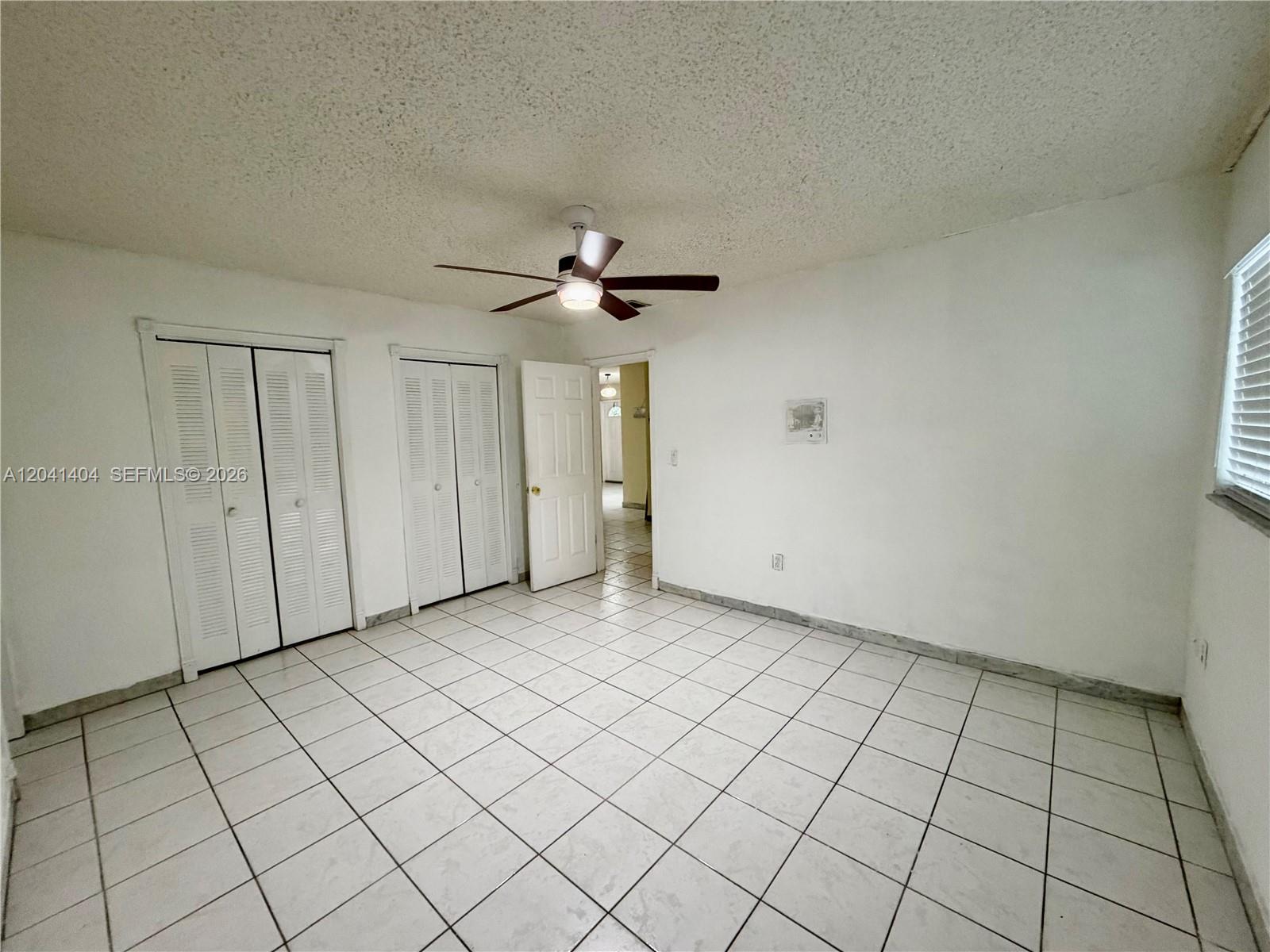 A bedroom features white walls, tiled floors, a ceiling fan, and two sets of closet doors — 913 NW 22nd Pl # 0, Miami FL 33125, MIAMI, FL