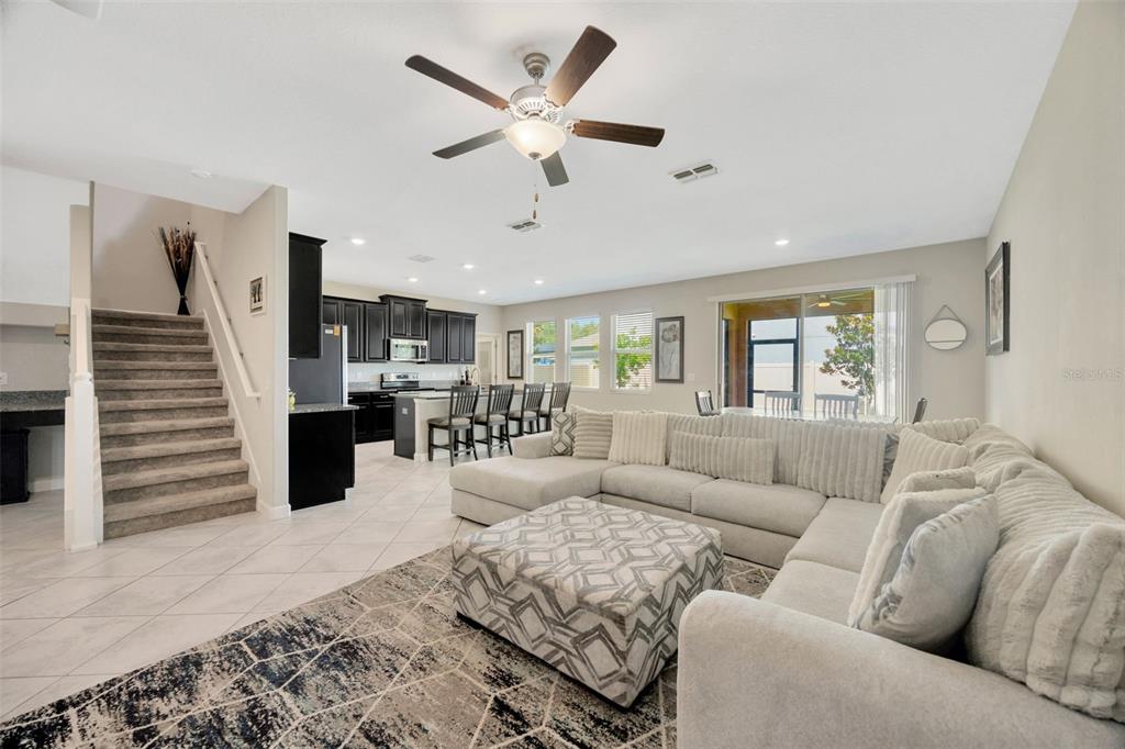 A living room with a sectional sofa and ottoman opens to a kitchen with dark cabinets — 11464 CHILLY WATER COURT, RIVERVIEW, FL