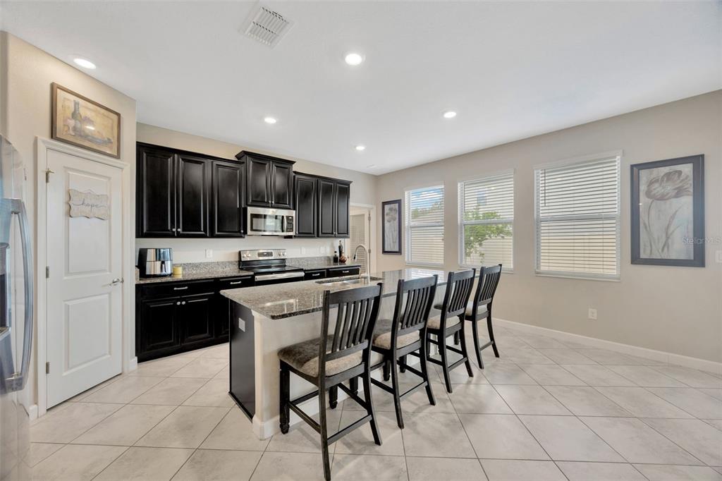 A kitchen features dark cabinets, granite countertops, a central island with bar seating, and tile flooring — 11464 CHILLY WATER COURT, RIVERVIEW, FL