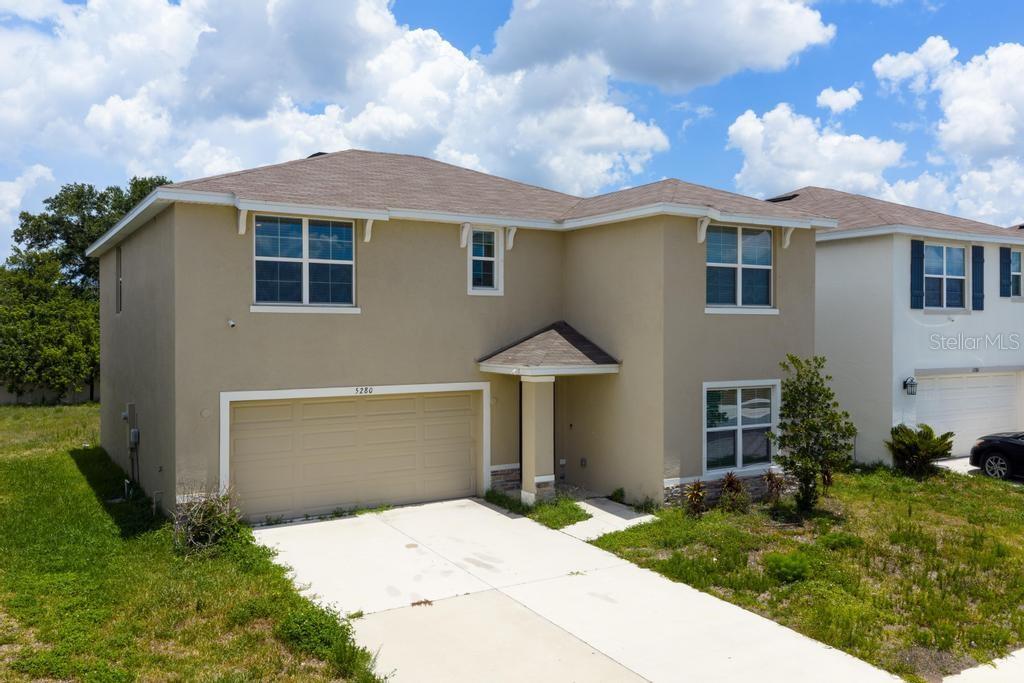 A two-story suburban house with a tan stucco exterior, a two-car garage, and a driveway — 5280 FIDDLE FIG AVENUE, WIMAUMA, FL