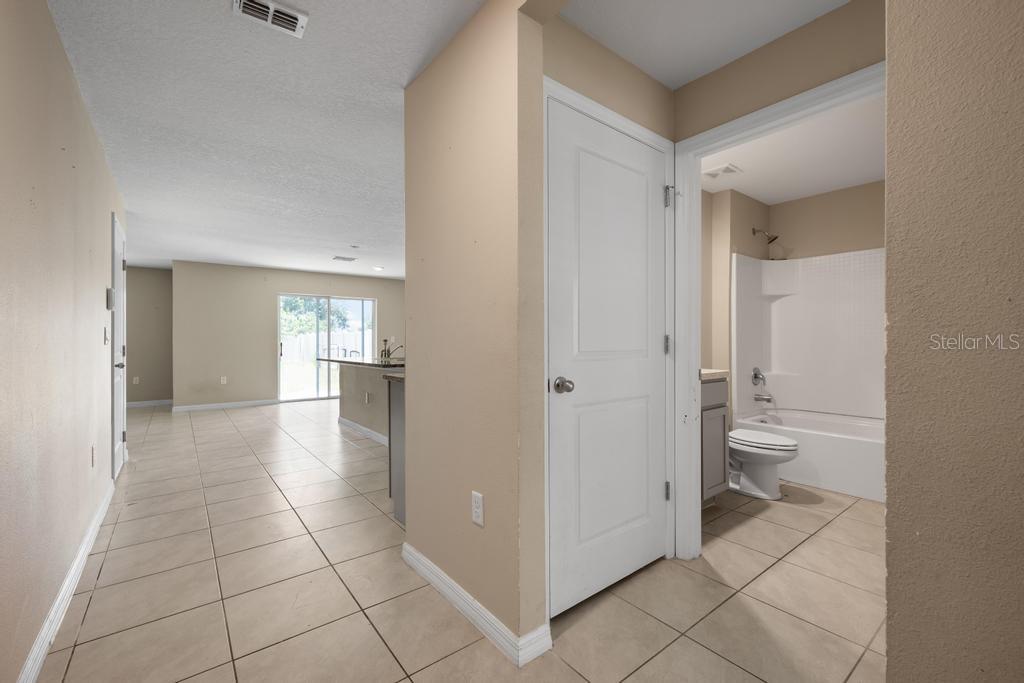 A tiled hallway leads to an open-concept kitchen and a bathroom with a tub — 5280 FIDDLE FIG AVENUE, WIMAUMA, FL