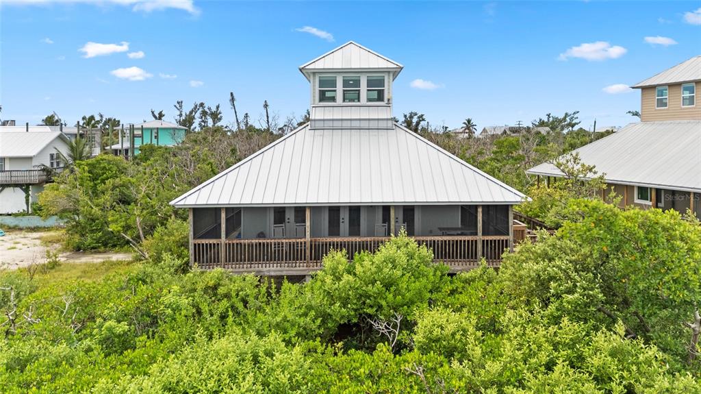 A stilt house with a metal roof and a screened-in porch sits among lush greenery — 8772 LITTLE GASPARILLA ISLAND, PLACIDA, FL