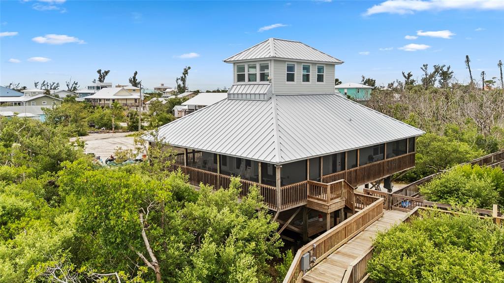 An elevated house with a metal roof and a cupola sits amidst dense green trees — 8772 LITTLE GASPARILLA ISLAND, PLACIDA, FL
