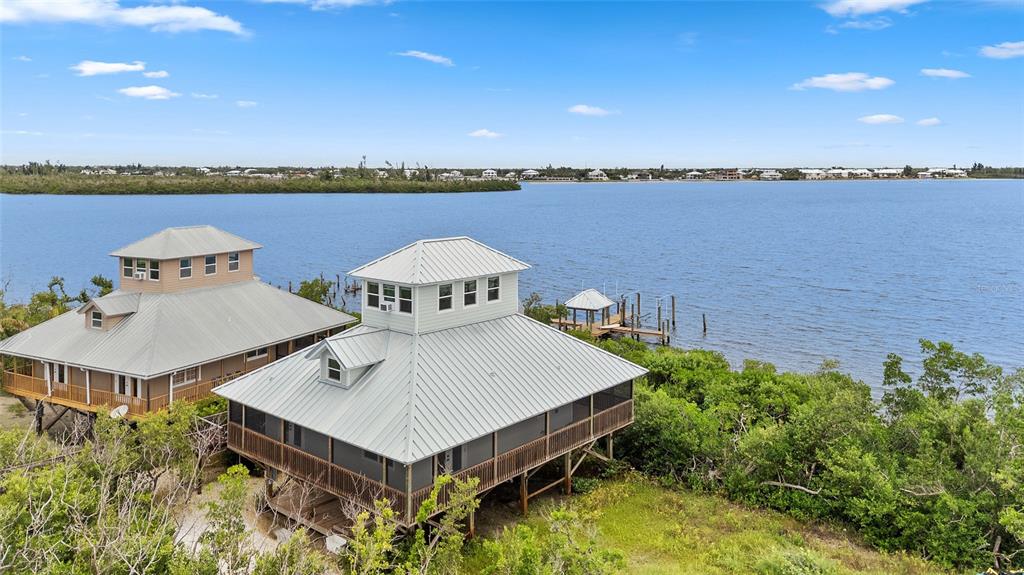 Two elevated houses with metal roofs sit along a waterfront with a private dock — 8772 LITTLE GASPARILLA ISLAND, PLACIDA, FL