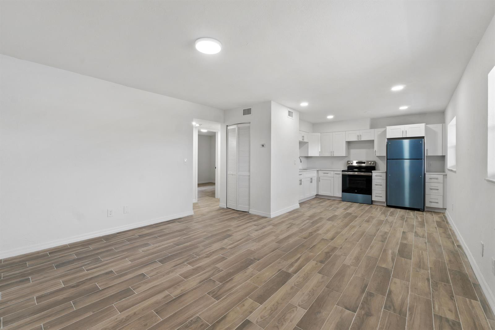 An open-concept kitchen and living area features white cabinets, stainless appliances, and wood-look flooring — 1301 Emerald Terrace # 8, Fort Pierce FL 34950, FORT PIERCE, FL