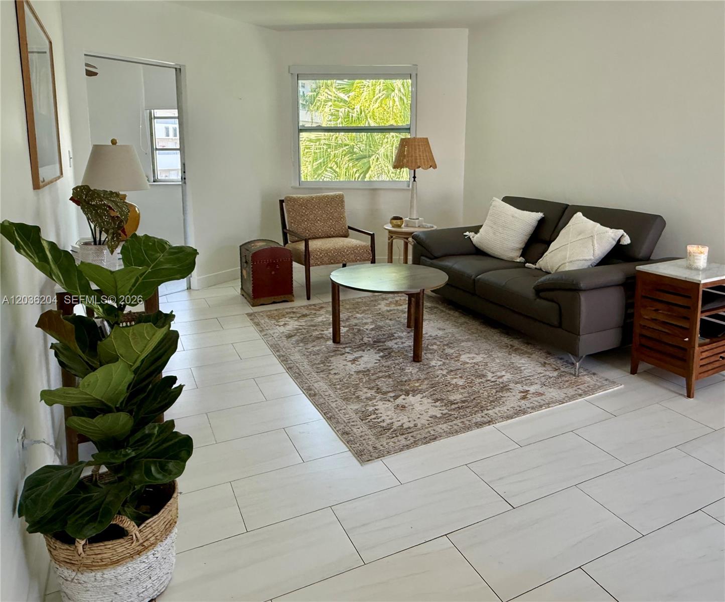A living room features white tile flooring, a dark sofa, an armchair, and a rug — 18750 NE 18th Ave # 251, Miami FL 33179, MIAMI, FL