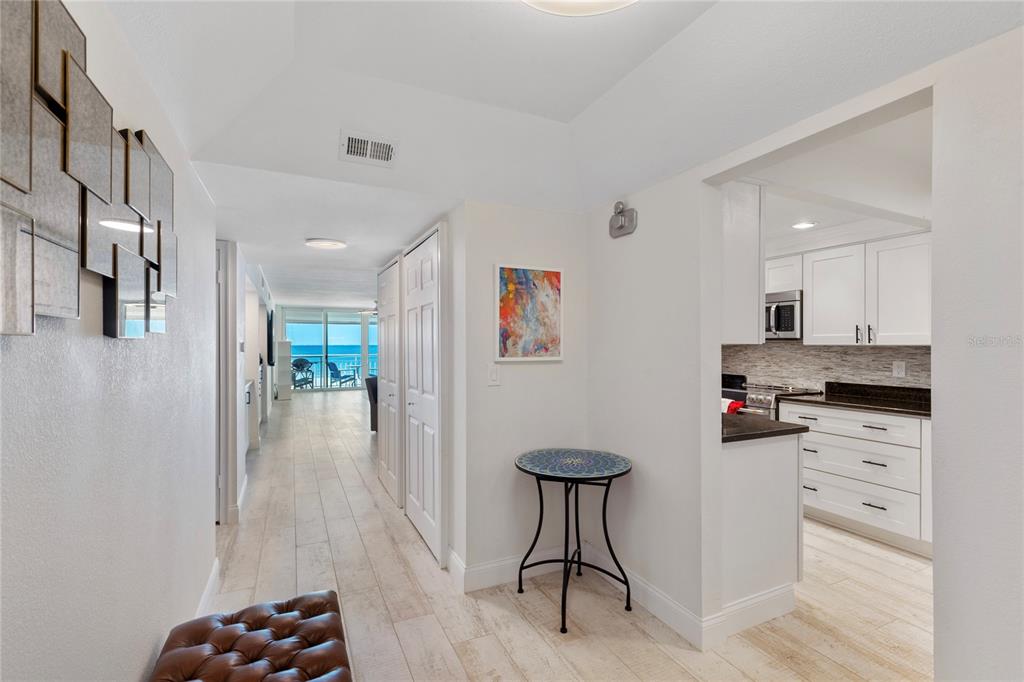 A hallway with light wood-look flooring leads toward a kitchen and a balcony with ocean views — 2900 GULF BOULEVARD UNIT 202, BELLEAIR BEACH, FL